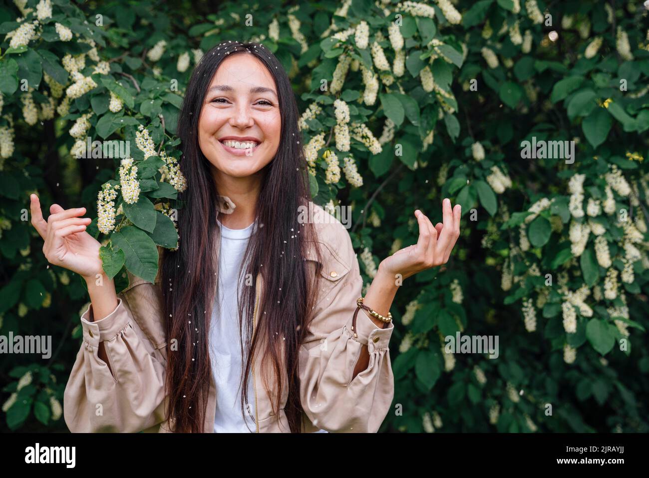 Lächelnde Frau mit gefallenen Blütenblättern auf den Haaren vor dem Baum Stockfoto