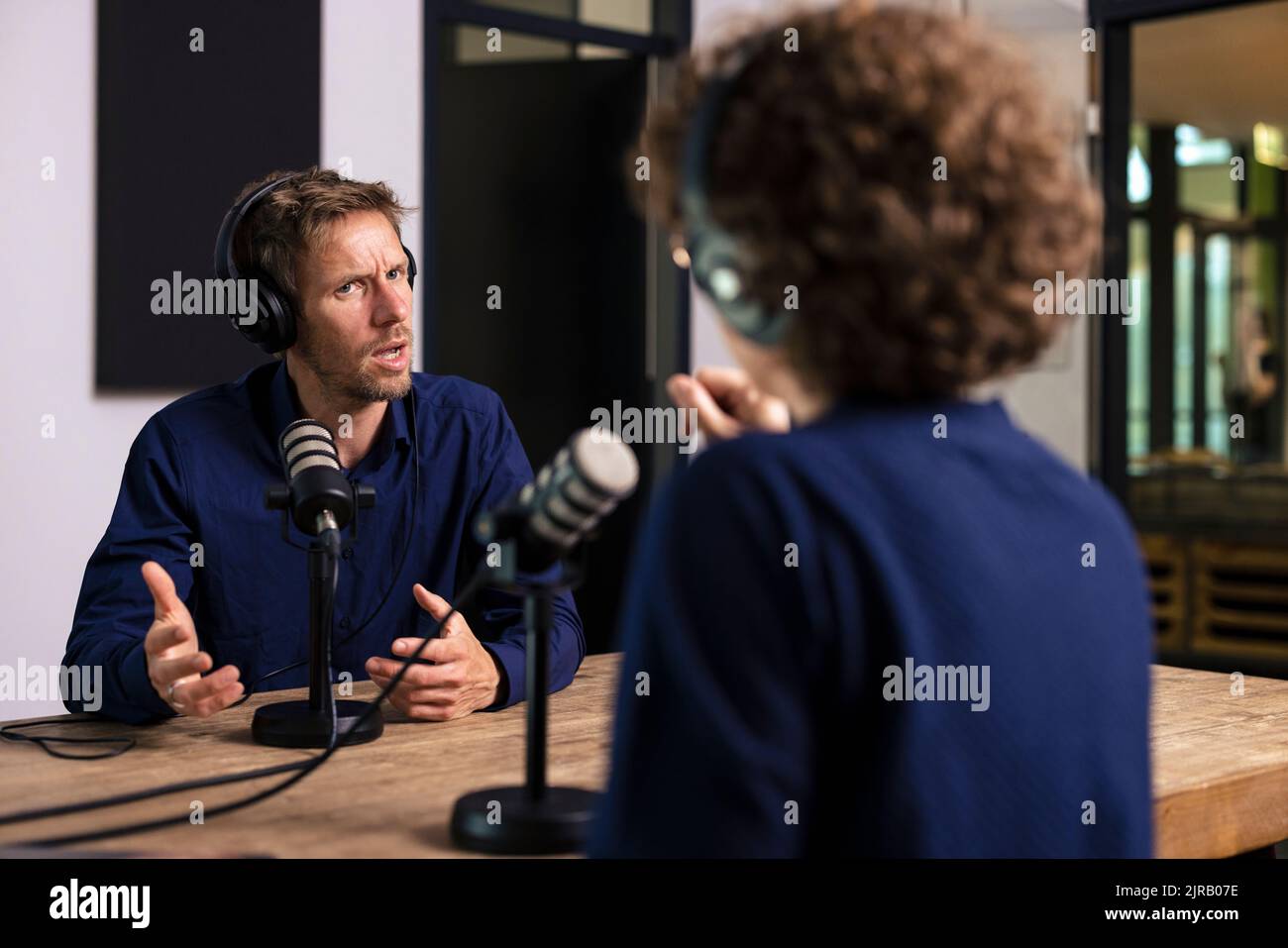 Gast gestikuliert im Gespräch mit Radio-DJ im Aufnahmestudio Stockfoto