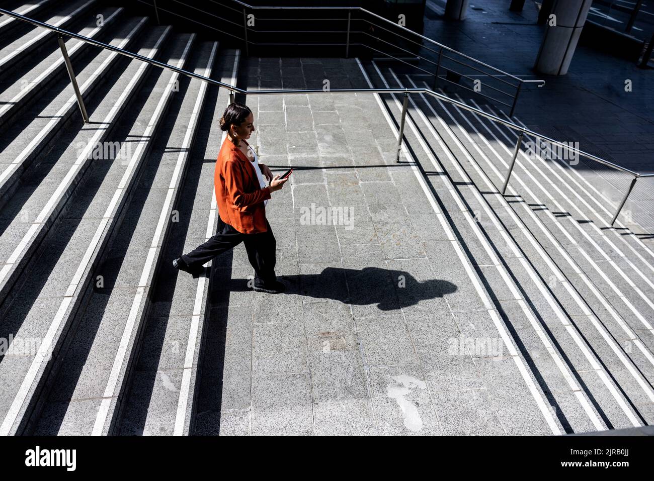 Geschäftsfrau mit Mobiltelefon, die sich auf der Treppe nach unten bewegt Stockfoto