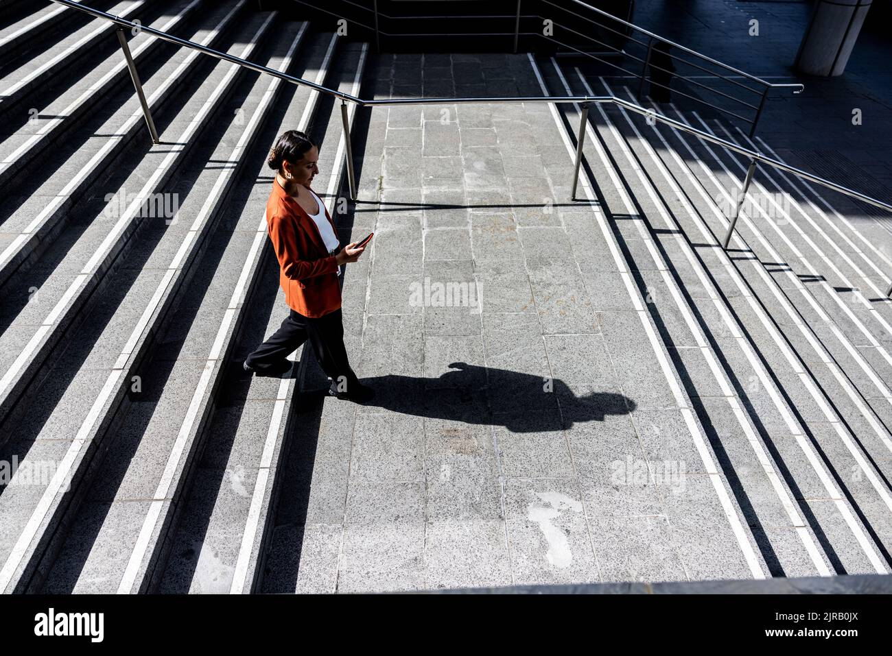 Geschäftsfrau, die ein Smartphone benutzt, das sich über die Treppe nach unten bewegt Stockfoto