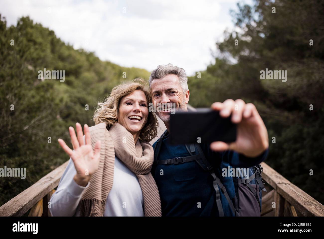 Glücklicher reifer Mann mit Frau, die Hand auf Smartphone winkt Stockfoto