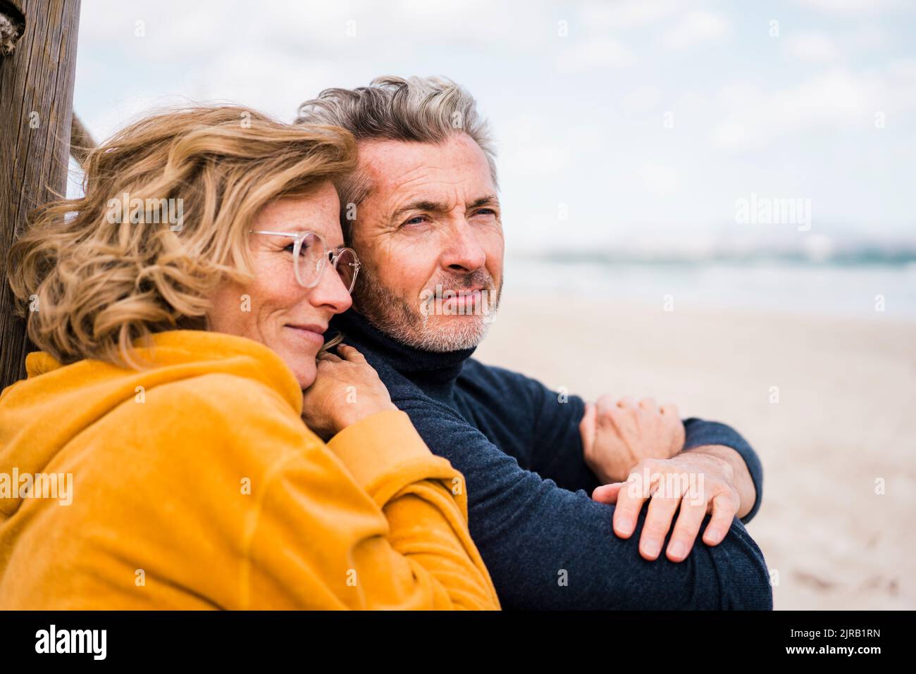 Lächelnde, reife Frau mit Brille, die den Urlaub mit dem Mann am Strand genießt Stockfoto