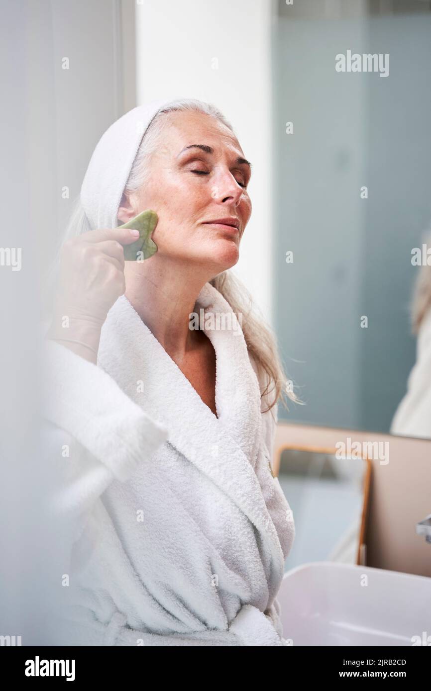 Wunderschöne Frau, die im Badezimmer mit Jadestein massiert Stockfoto