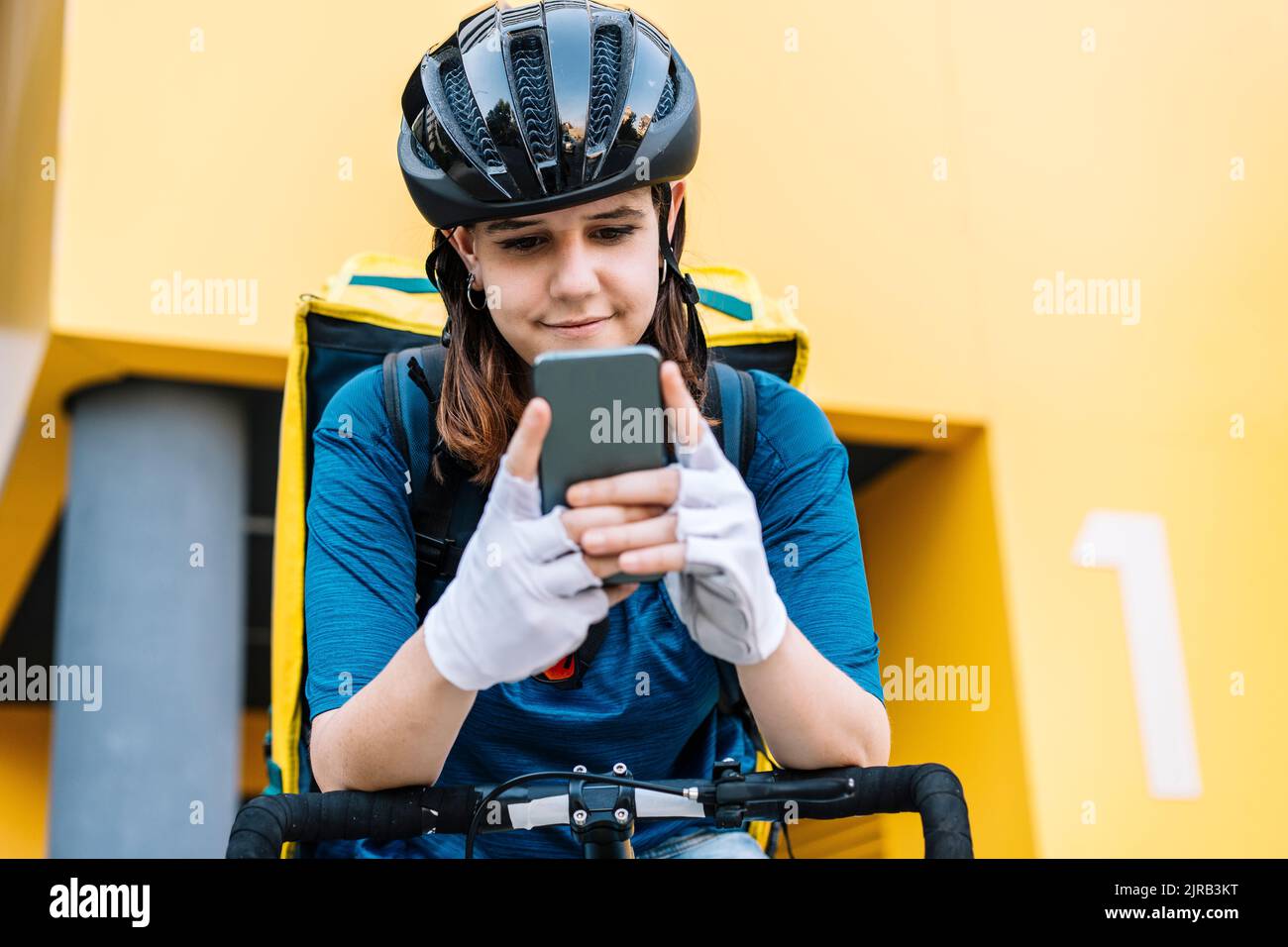Lächelnde Lieferung Frau trägt Helm Textnachrichten über Smartphone Stockfoto