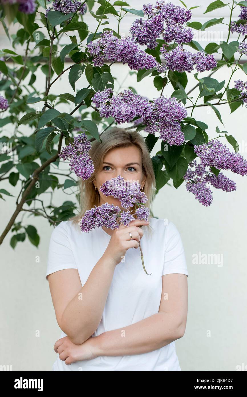 Nachdenkliche reife Frau, die vor der Wand lilafarbe Blumen riecht Stockfoto
