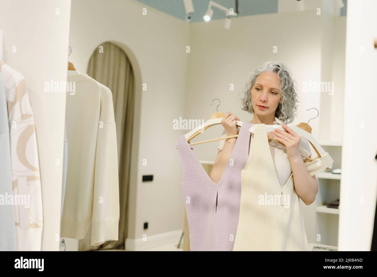 Frau, die im Spiegel schaut und Kleider im Laden anprobiert Stockfoto