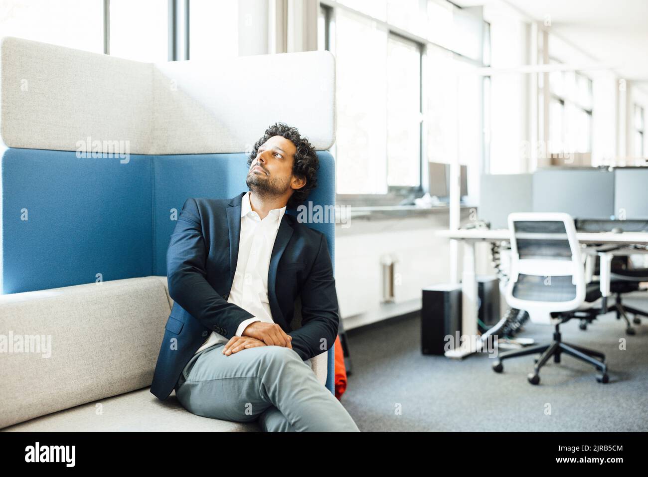 Nachdenklicher Geschäftsmann, der am Arbeitsplatz auf dem Sofa sitzt Stockfoto