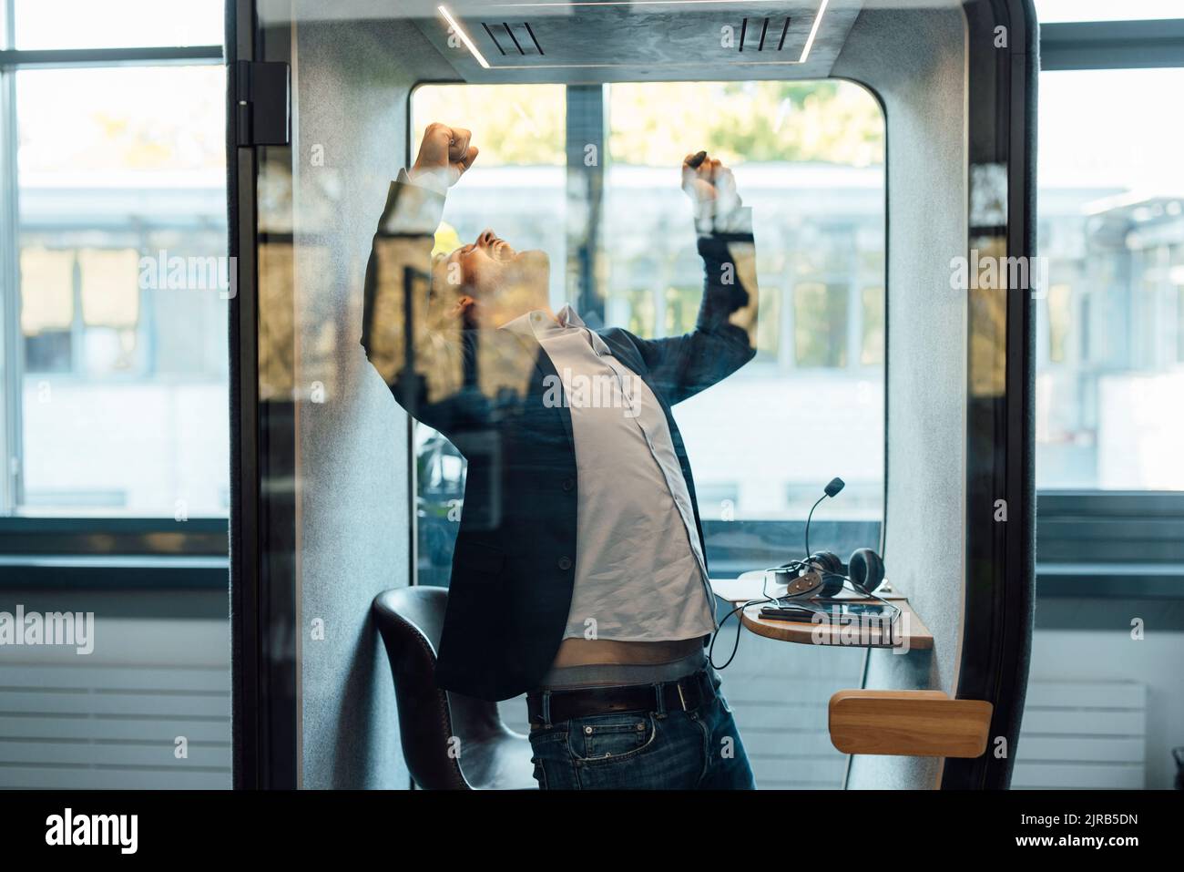 Erfolgreicher Geschäftsmann, der am Arbeitsplatz die Fäuste in einer schallisolierten Kabine hält Stockfoto