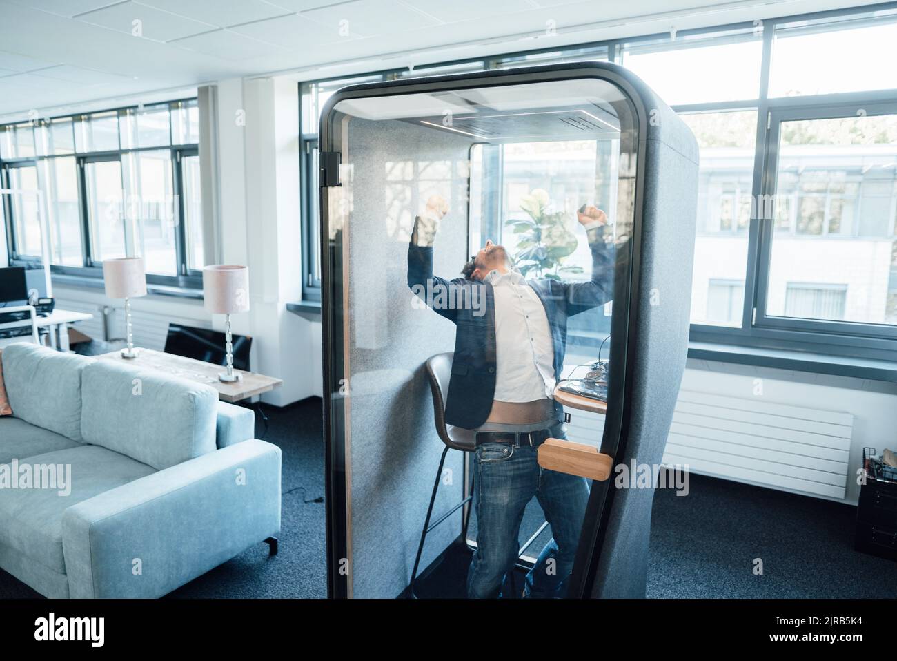 Erfolgreicher Geschäftsmann, der am Arbeitsplatz die Fäuste in einer schallisolierten Kabine hält Stockfoto