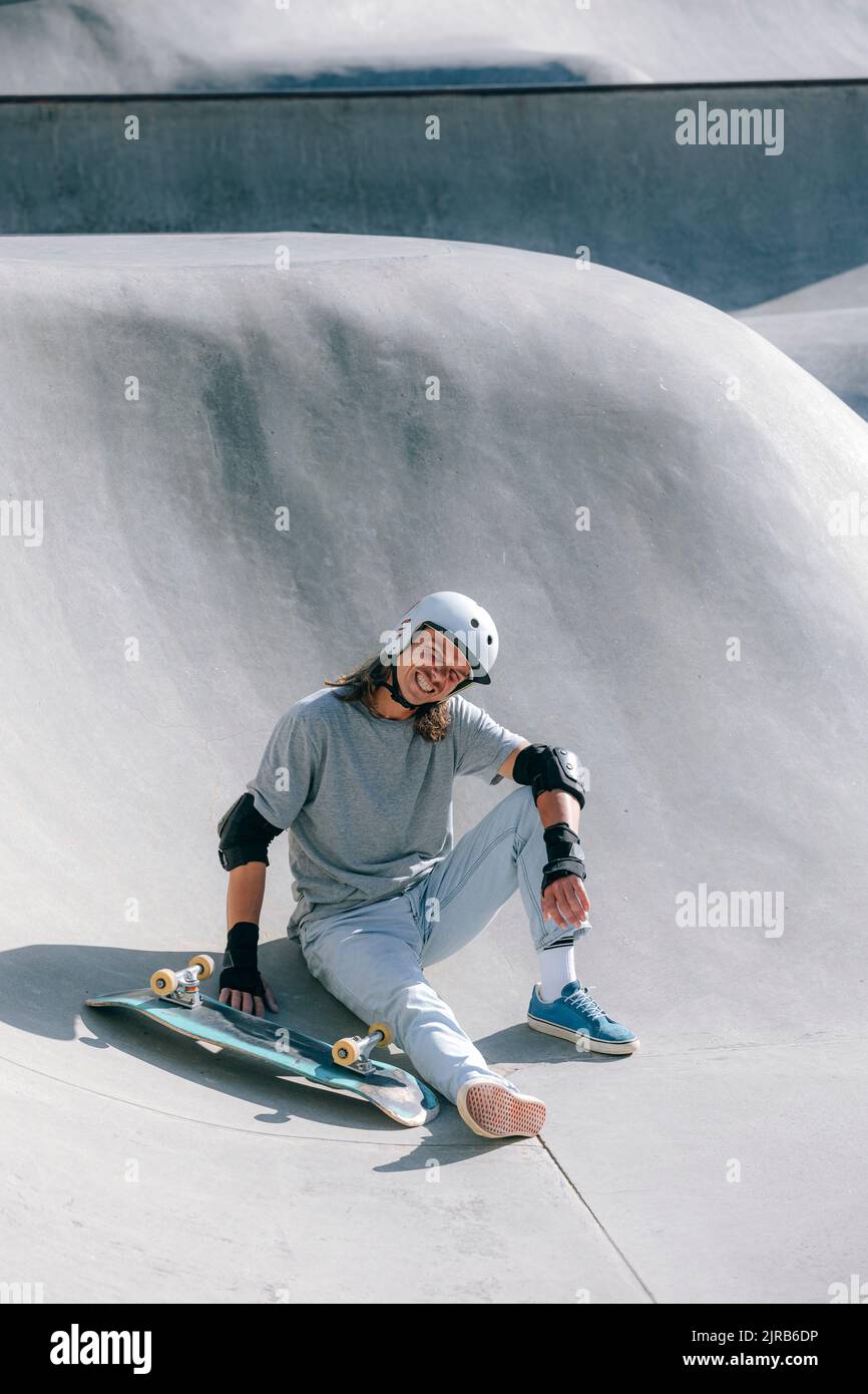 Lächelnder Mann, der am sonnigen Tag im Skateboard im Skatepark sitzt Stockfoto