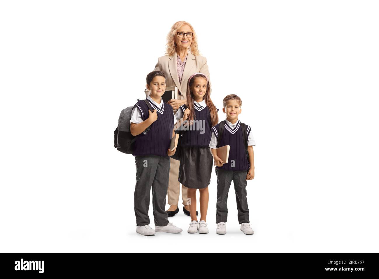 Lehrerin mit drei Schulkindern in Uniformen, die isoliert auf weißem Hintergrund stehen und die Kamera betrachten Stockfoto