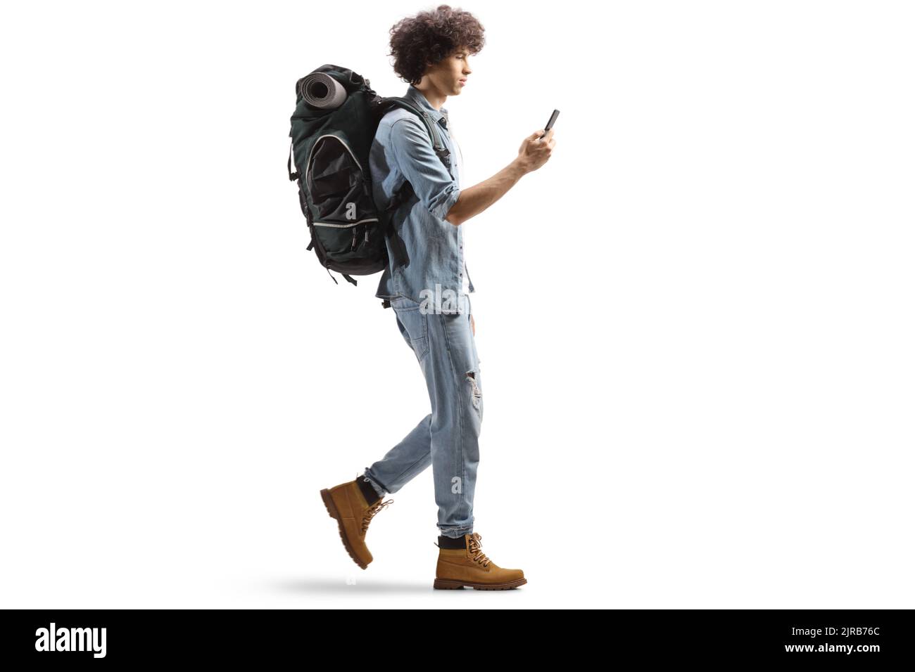 In voller Länge Profilaufnahme eines jungen männlichen Backpackers, der mit einem Smartphone auf weißem Hintergrund isoliert unterwegs ist Stockfoto