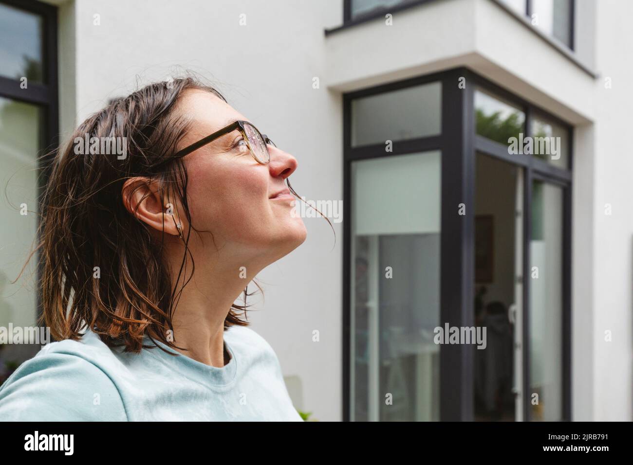 Frau mit nassem Haar, die das Wetter vor dem Haus bewundert Stockfoto