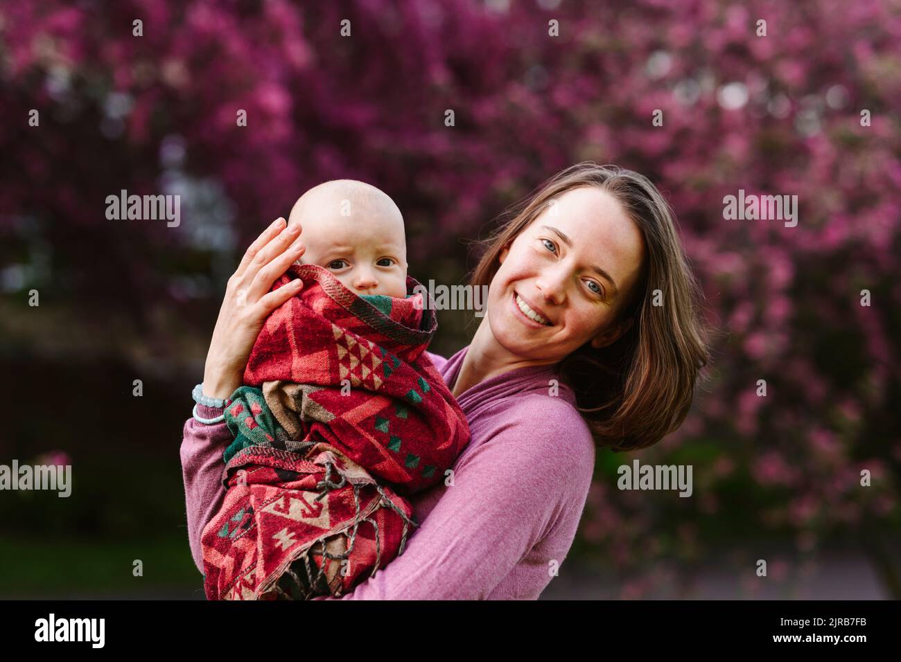 Glückliche Frau, die einen kleinen Jungen in einer Decke im Garten trägt Stockfoto