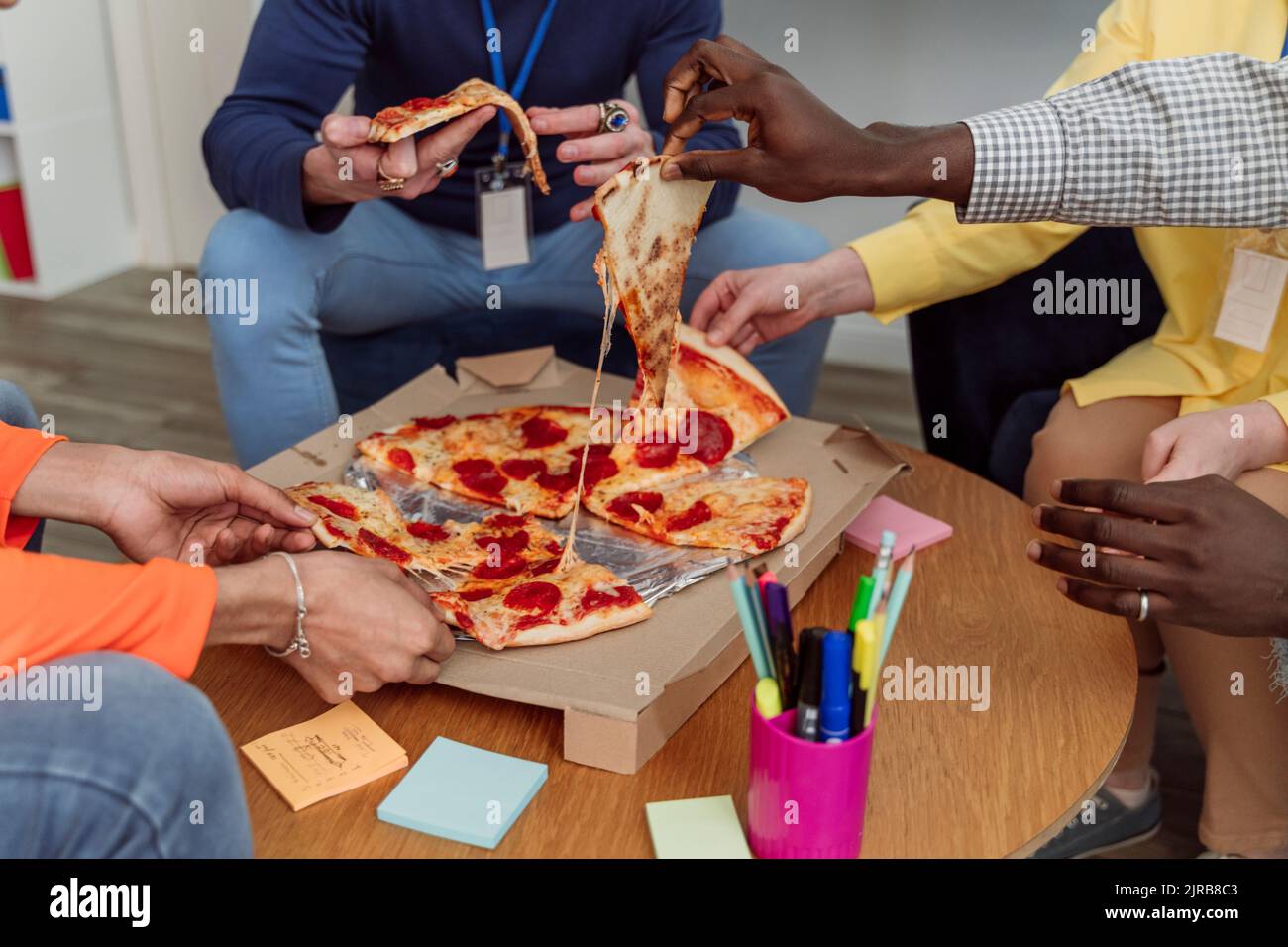 Hände von Geschäftskollegen, die Pizzastücke im Büro halten Stockfoto