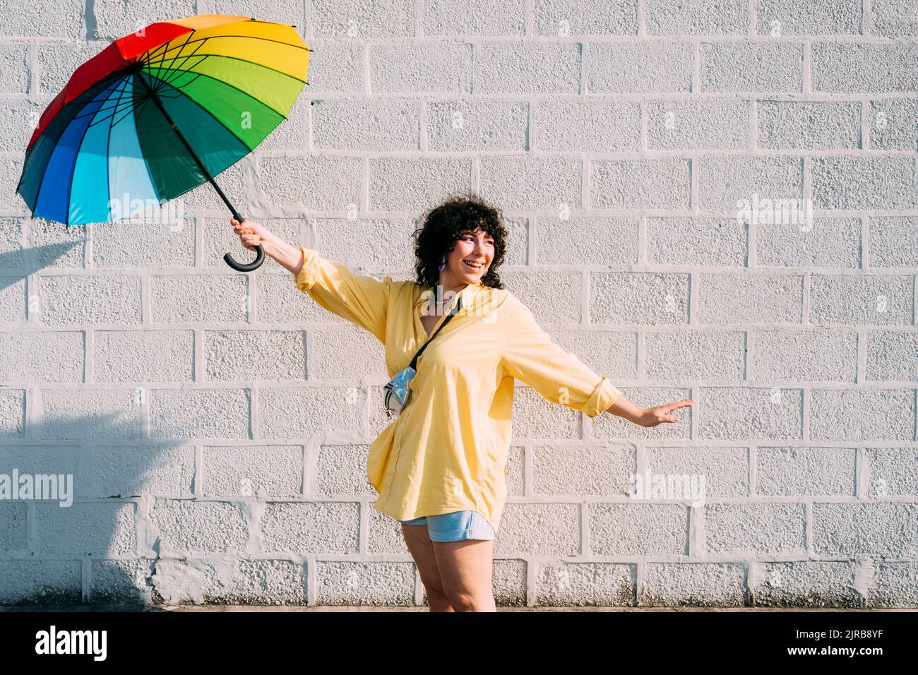 Glückliche Frau mit Regenbogenschirm vor der Wand posiert Stockfoto