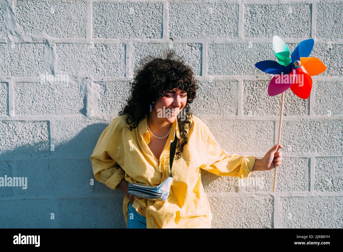 Frau mit Windrad-Spielzeug lachend vor der Steinmauer Stockfoto
