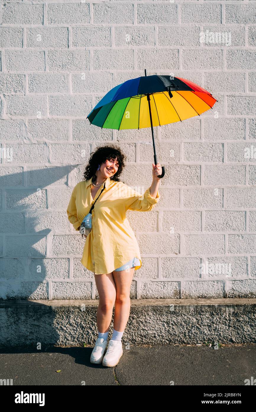 Lächelnde Frau mit Regenbogenschirm vor der Wand Stockfoto