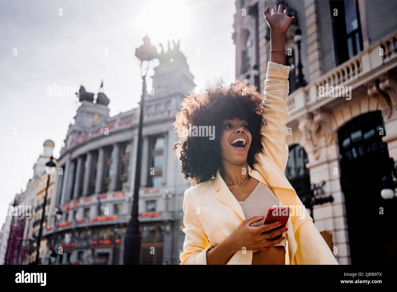 Aufgeregt Frau mit Smartphone winkt in der Stadt Stockfoto