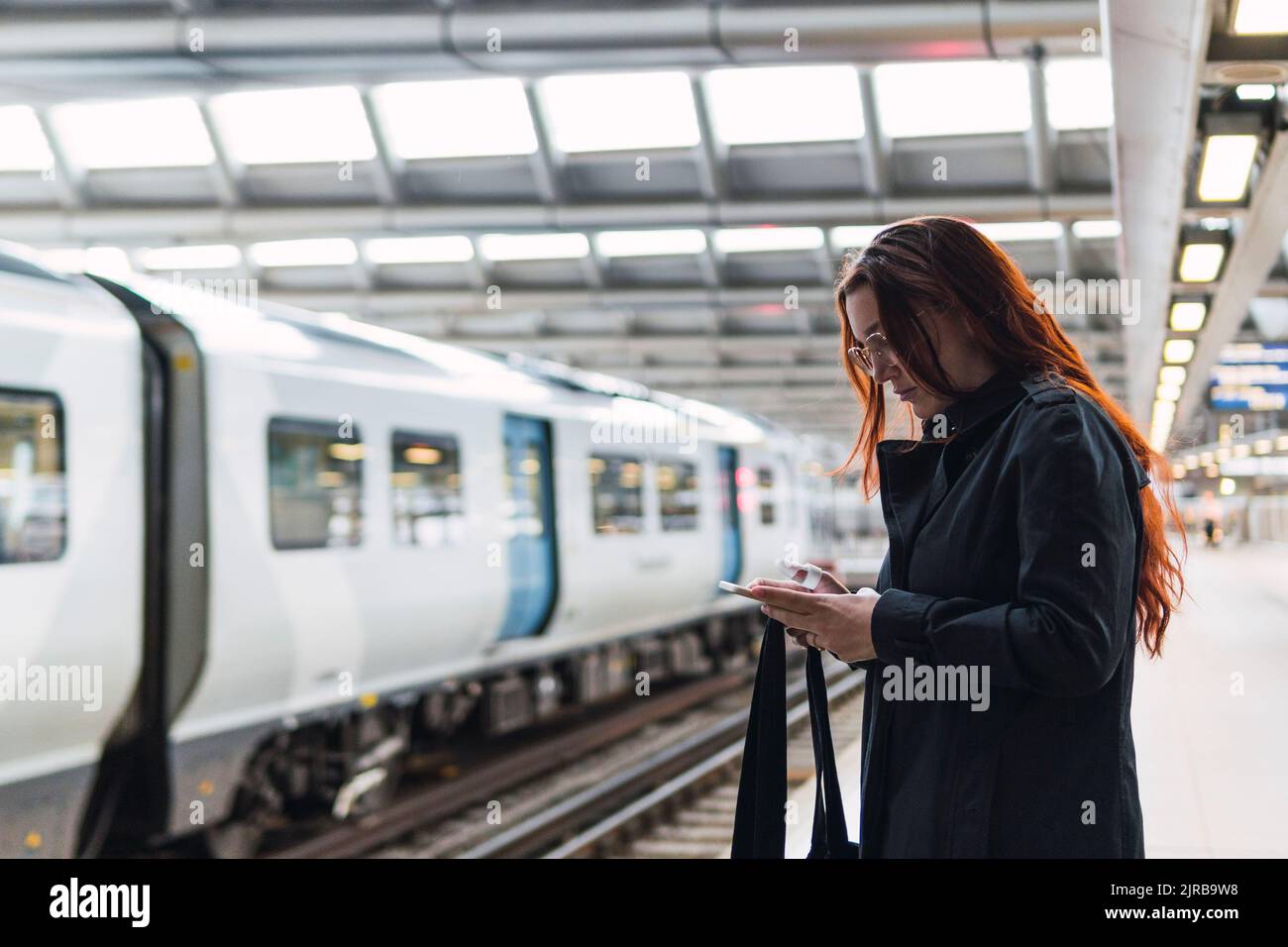 Rotschopf Frau mit Smartphone am Bahnhofssteig Stockfoto