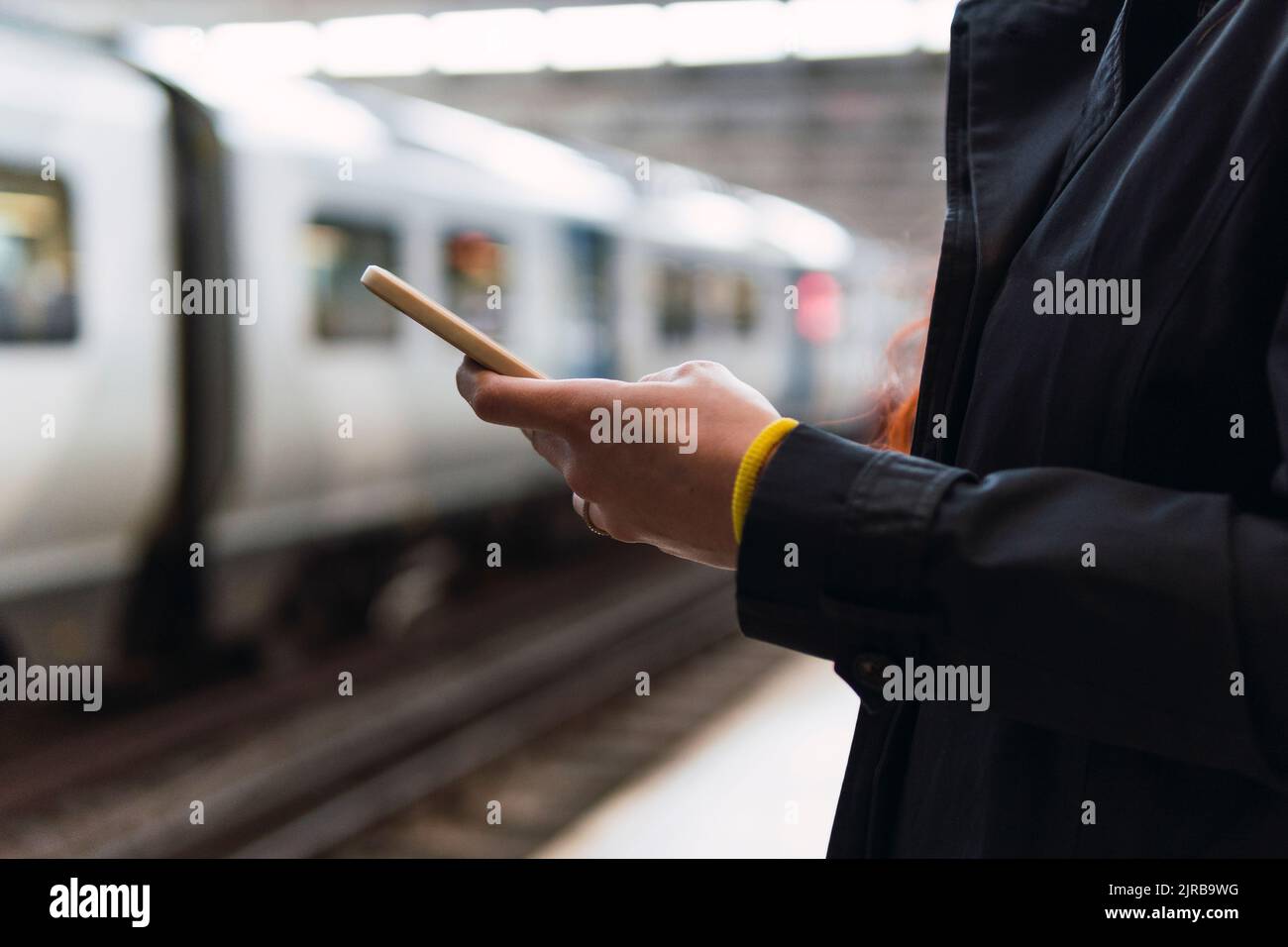 Hände einer Frau, die am Bahnhofssteig ein Mobiltelefon benutzt Stockfoto