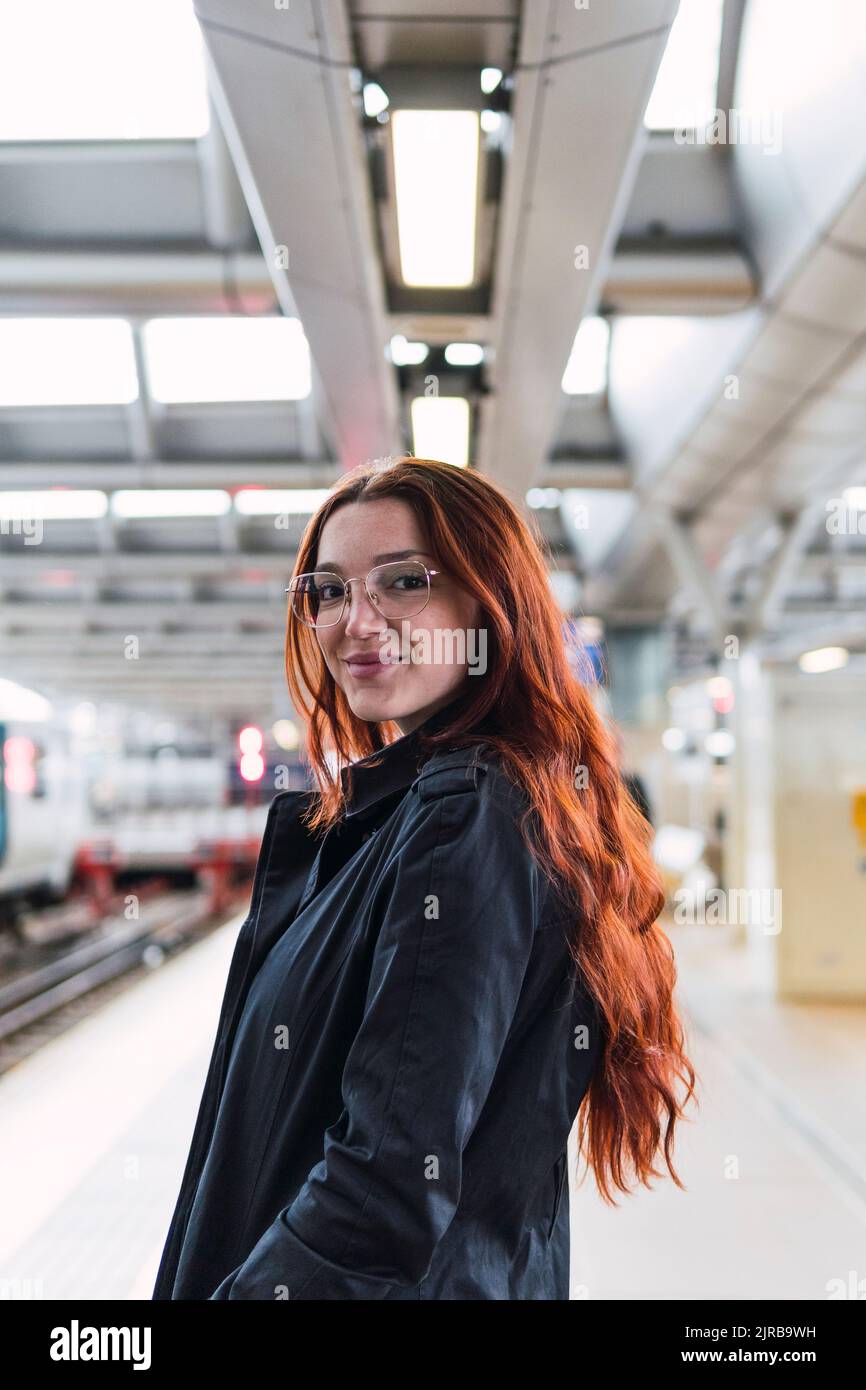 Glückliche Rothaarige Frau, die am Bahnhofssteig steht Stockfoto