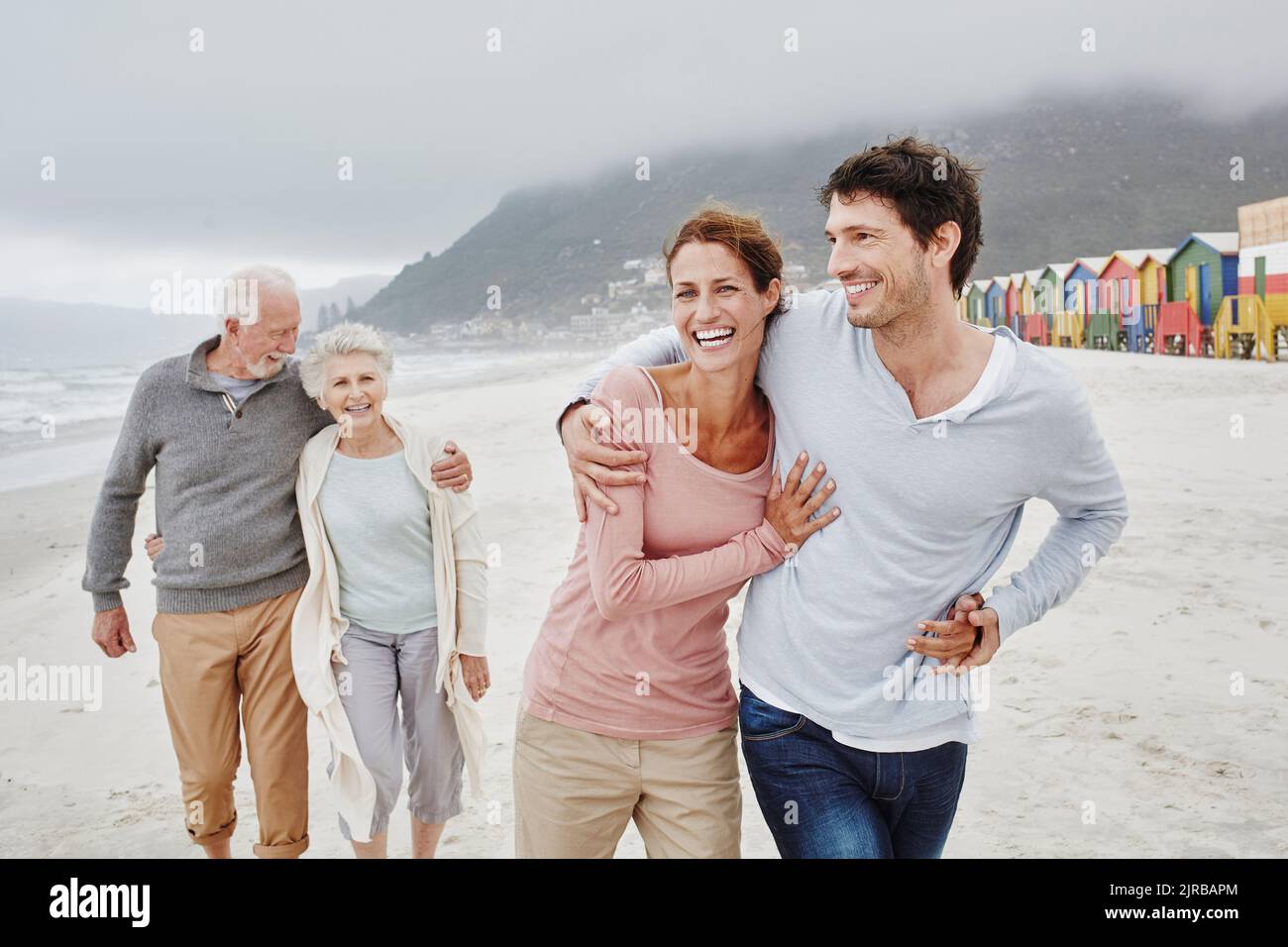Erwachsenes Paar, das mit älteren Eltern am Strand spazieren geht Stockfoto