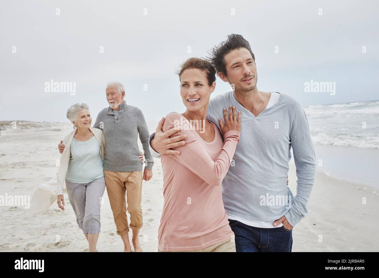 Erwachsenes Paar, das mit älteren Eltern am Strand spazieren geht Stockfoto