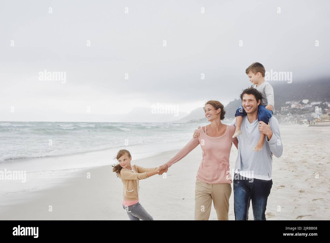 Eltern gehen mit zwei Kindern am Strand und tragen ihren Sohn auf den ...