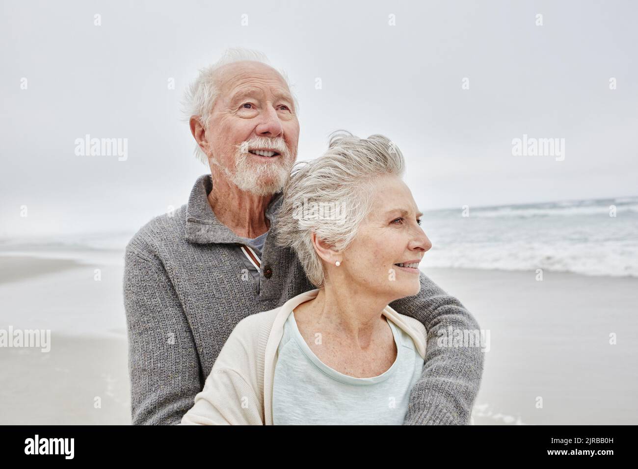 Glückliches Ehepaar, das lächelnd am windigen Strand steht Stockfoto