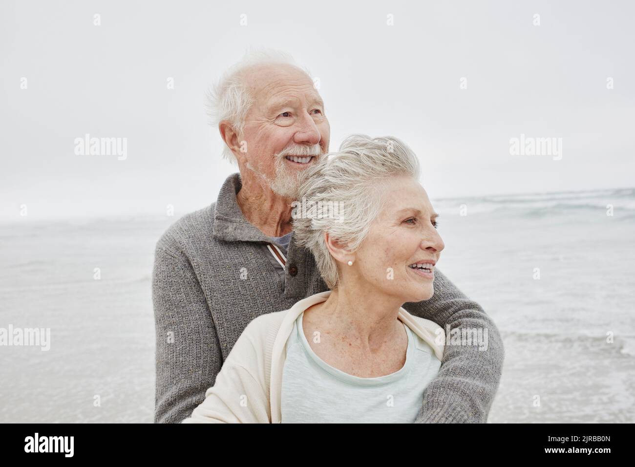 Glückliches Ehepaar, das lächelnd am windigen Strand steht Stockfoto