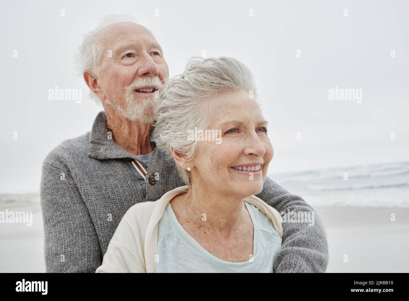Glückliches Ehepaar, das lächelnd am windigen Strand steht Stockfoto