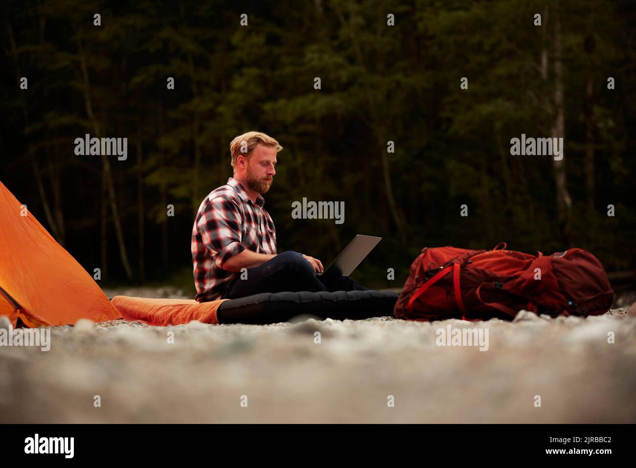 Geschäftsmann mit Laptop auf aufblasbarer Matratze auf dem Campingplatz sitzen Stockfoto