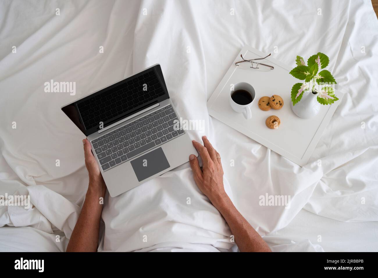 Hände eines Mannes mit Laptop und Frühstück auf dem Bett Stockfoto
