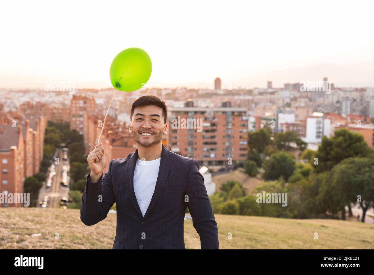 Glücklicher junger Geschäftsmann mit einem grünen Ballon, der auf einem Hügel steht Stockfoto