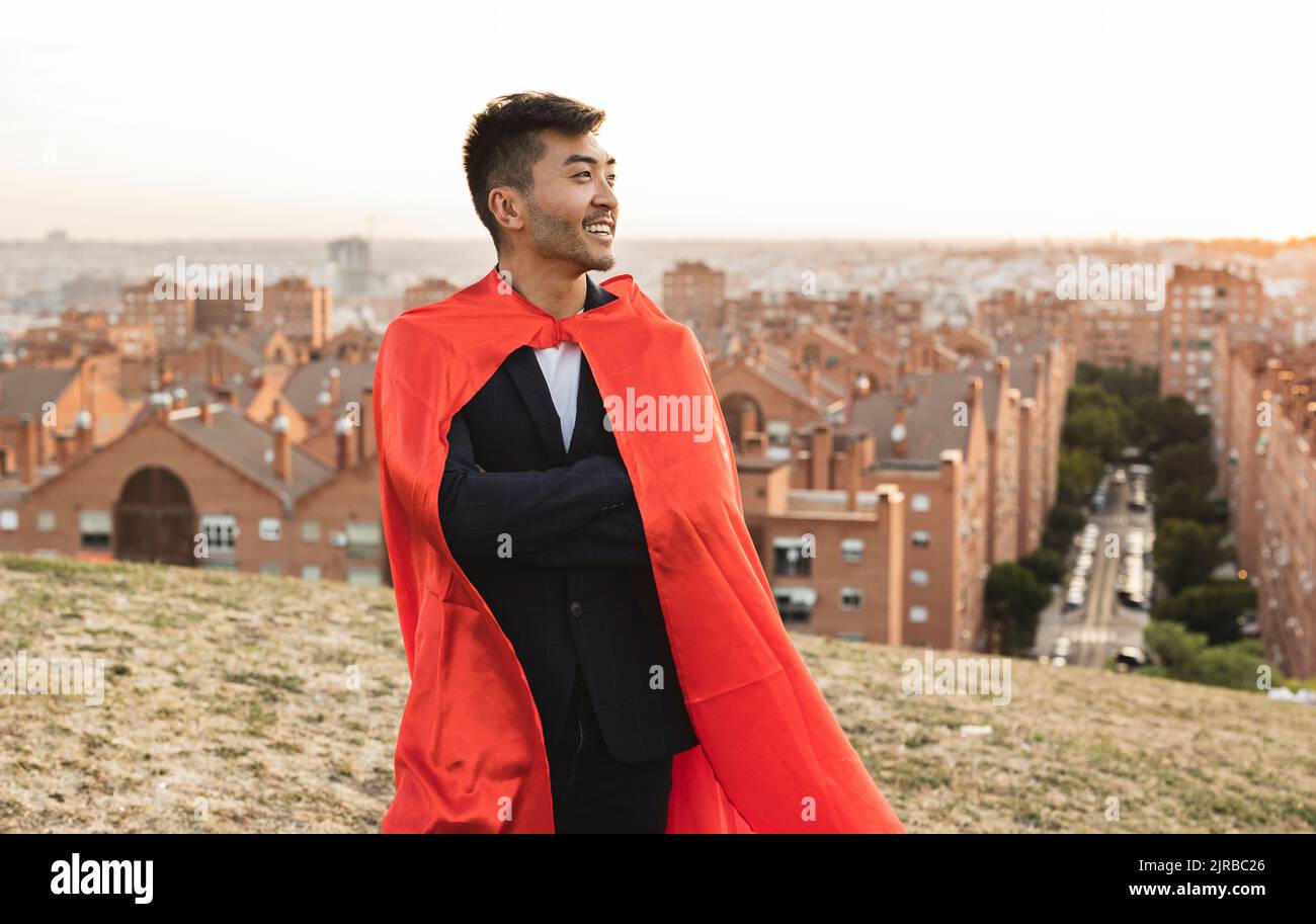 Glücklicher junger Geschäftsmann mit rotem Superhelden-Umhang auf einem Hügel Stockfoto