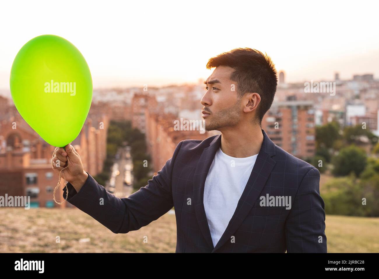 Nachdenklicher junger Geschäftsmann mit Blick auf den grünen Ballon Stockfoto
