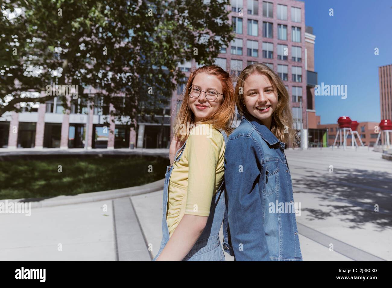 Lächelnde junge Freunde stehen auf dem Fußweg zurück an den Rücken Stockfoto