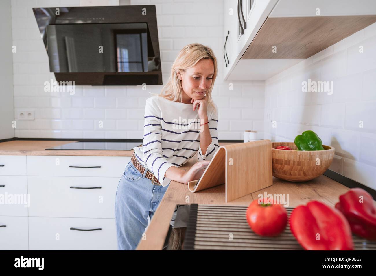 Junge Frau mit der Hand am Kinn beobachten Rezept auf Tablet-PC in der Küche zu Hause Stockfoto