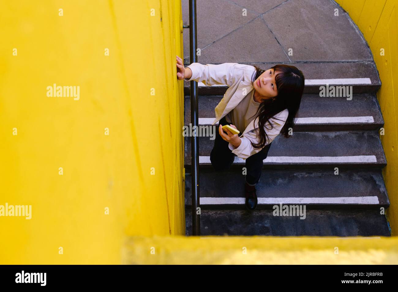 Junge Frau mit Smartphone auf der Treppe nach oben schauen Stockfoto