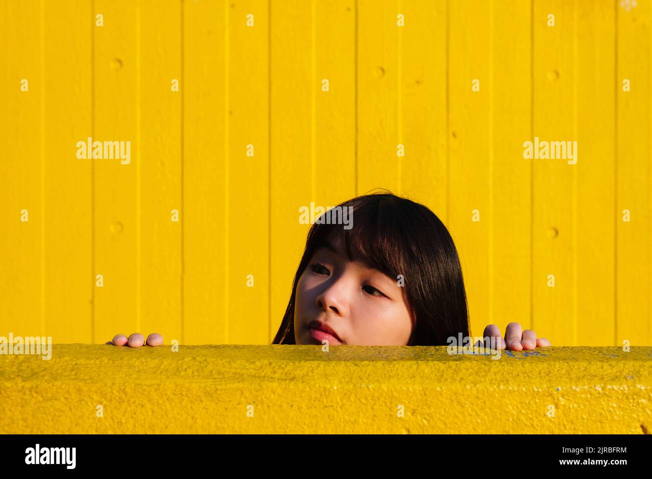 Junge Frau guckt von der gelben Wand Stockfoto