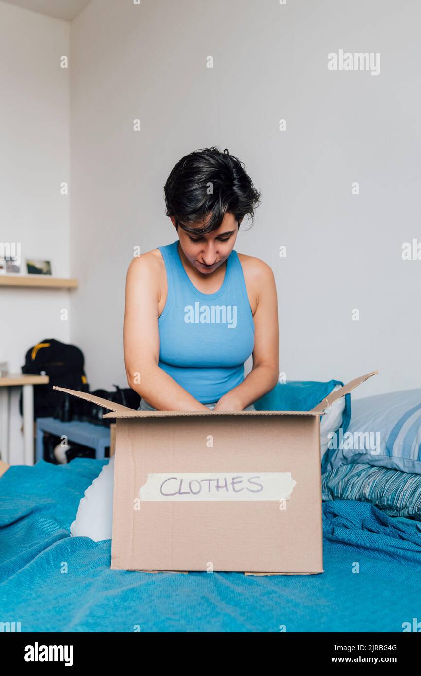 Junge Frau Verpackung Box für Kleidung Spende auf Bett zu Hause Stockfoto