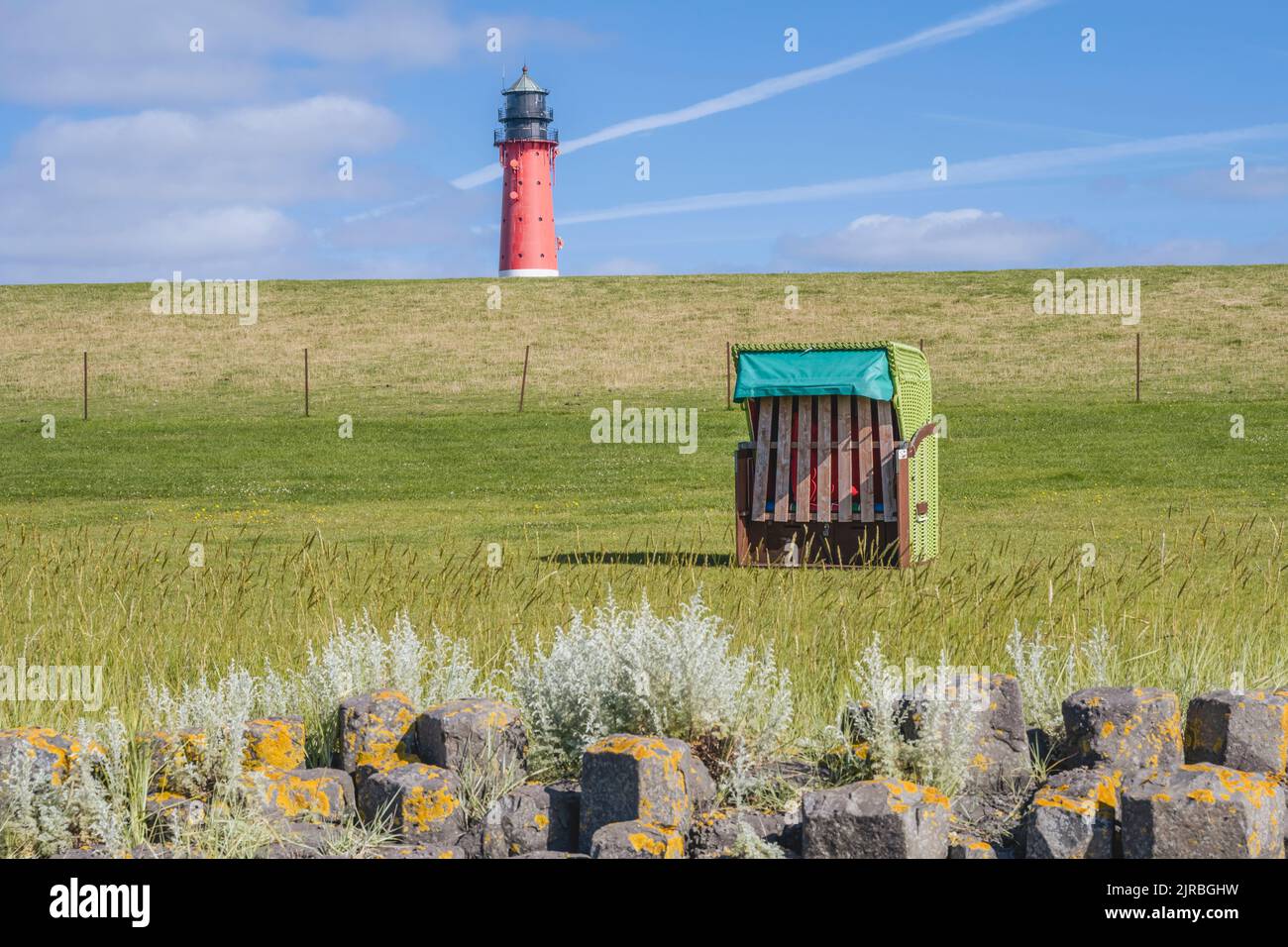 Deutschland, Schleswig-Holstein, Pellworm, Hooded Beach Chair mit Felsformation im Vordergrund und Pellworm Lighthouse im Hintergrund Stockfoto
