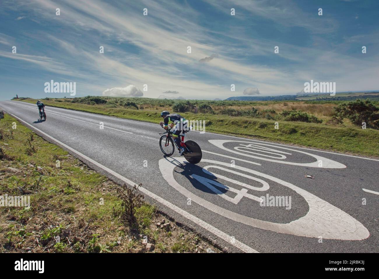 7. August 22 Gower Swansea Wales UK Triathlon Ironman Cycling Event „Over the Limit“ Radfahrer überqueren Straße gemalt Geschwindigkeitsbegrenzung Schild mit Mitbewerber voraus Stockfoto