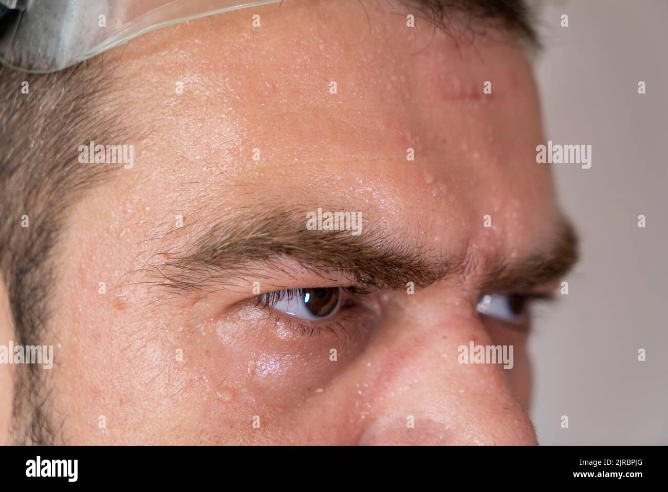 Selektiver Fokus, Nahaufnahme eines verschwitzten, erschöpften Männergesichts mit Markierungen der Sicherheitsausrüstung. Stockfoto