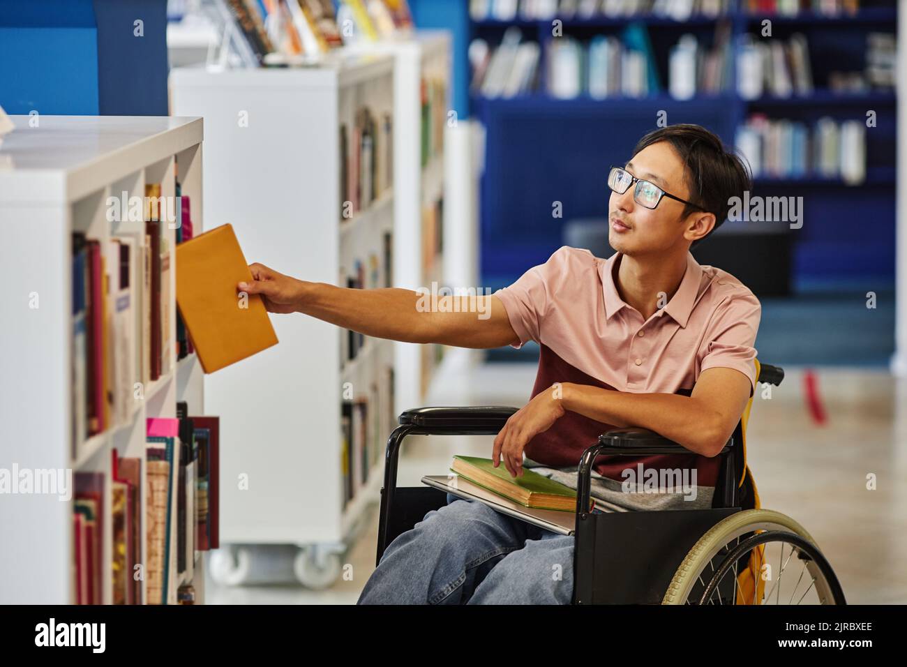 Porträt eines asiatischen Studenten mit Behinderung bei der Auswahl von Büchern in der Universitätsbibliothek mit barrierefreien Funktionen Stockfoto