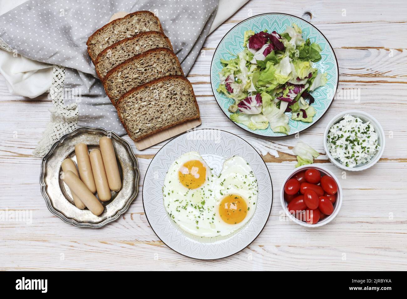 Teller mit Spiegeleiern, Brot, Salat, Wurst und Quark auf braunem Holztisch, Kopierplatz. Stockfoto