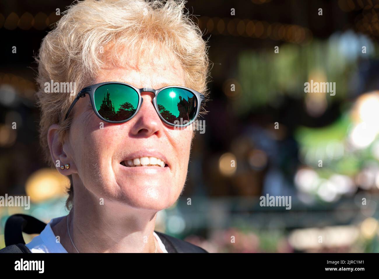 Eine weibliche Besucherin des Disneyland Parks, Paris, Frankreich. Sie blickt auf das Dornröschenschloss, was sich in ihrer Oakley-Sonnenbrille widerspiegelt Stockfoto