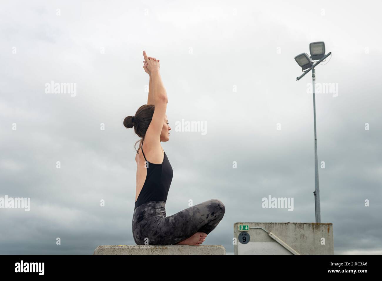 Junge Fitness-Frau meditiert in Lotusposition sitzend, städtischer Hintergrund. Sportliches Mädchen, das Yoga macht. Stockfoto
