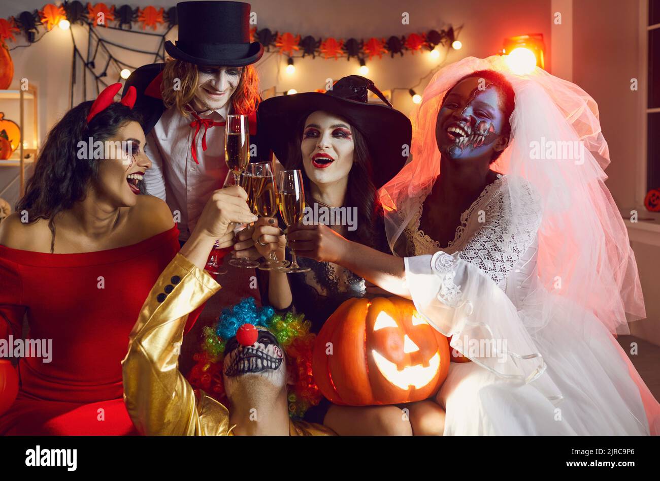 Eine Gruppe glücklicher junger Menschen in gruseligen Kostümen trinkt Champagner auf der Halloween-Party Stockfoto
